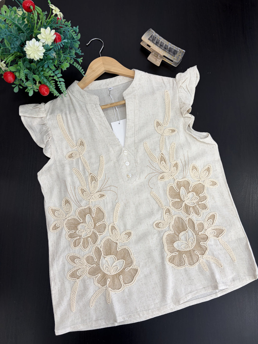 White sleeveless top with floral embroidery on a dark background