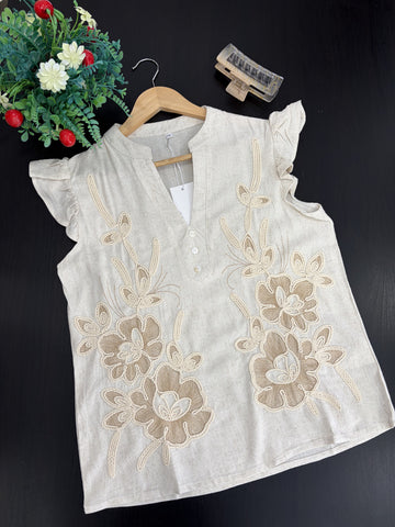 White sleeveless top with floral embroidery on a dark background