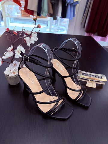 Black strappy sandals on a dark surface with decorative flowers and a hair clip.