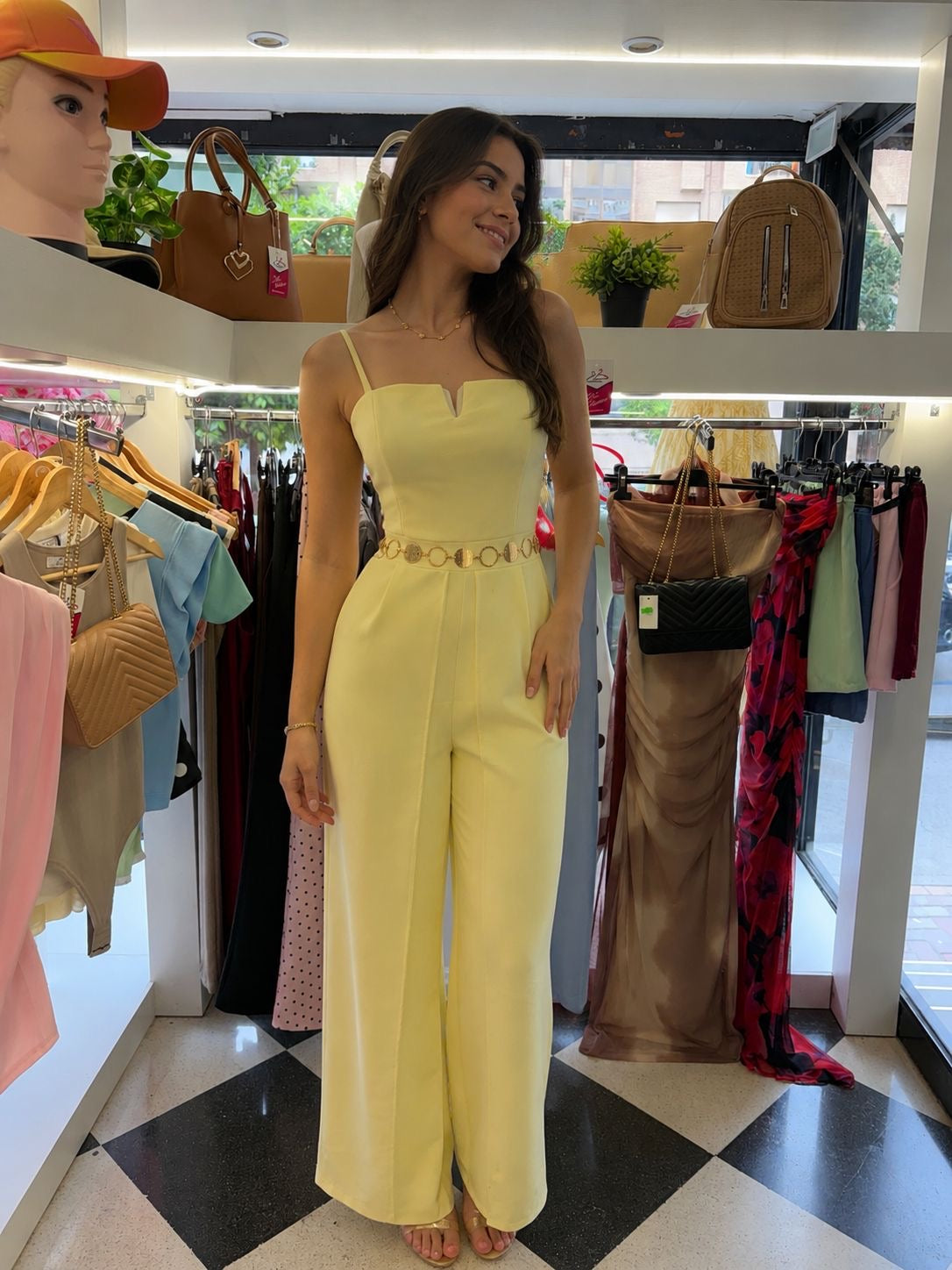 Woman in a yellow dress standing in a clothing store with racks and bags in the background.