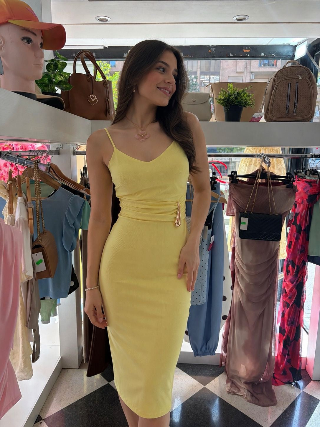 Woman in a yellow dress standing in a clothing store with racks of clothes and bags in the background.